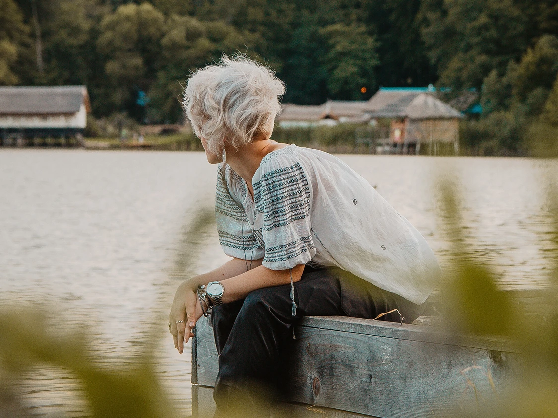 Frau sitzt am see und schaut hinaus